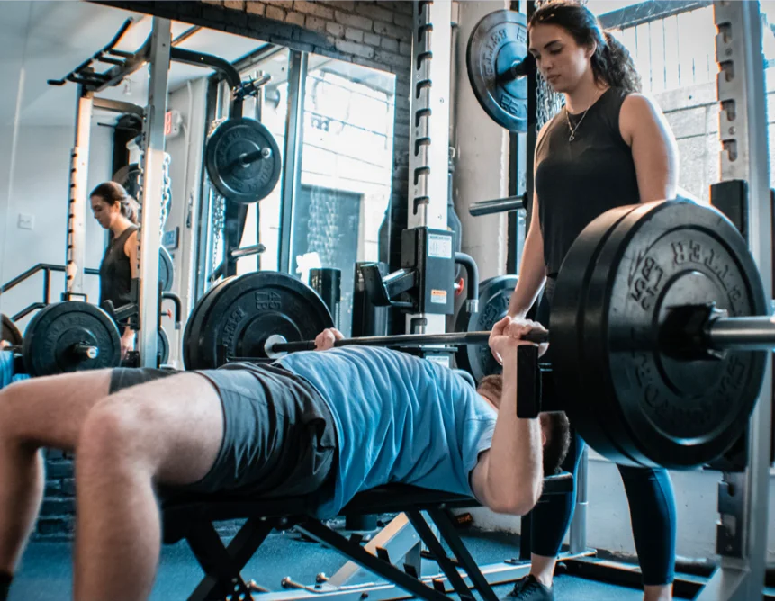 Man lifting a barbell weight with the supervision of the female personal trainer at Power lift studio